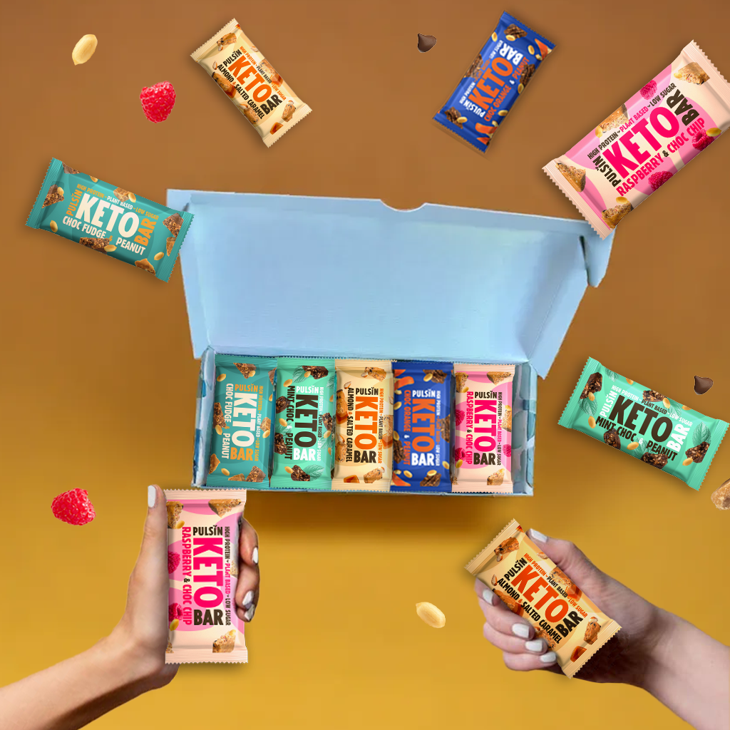 Assorted keto bars in an open box with hands holding different bars on a yellow and brown gradient background.